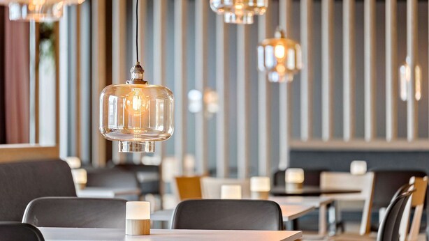 Interior de restaurante con lámparas colgantes, mesas y sillas.
