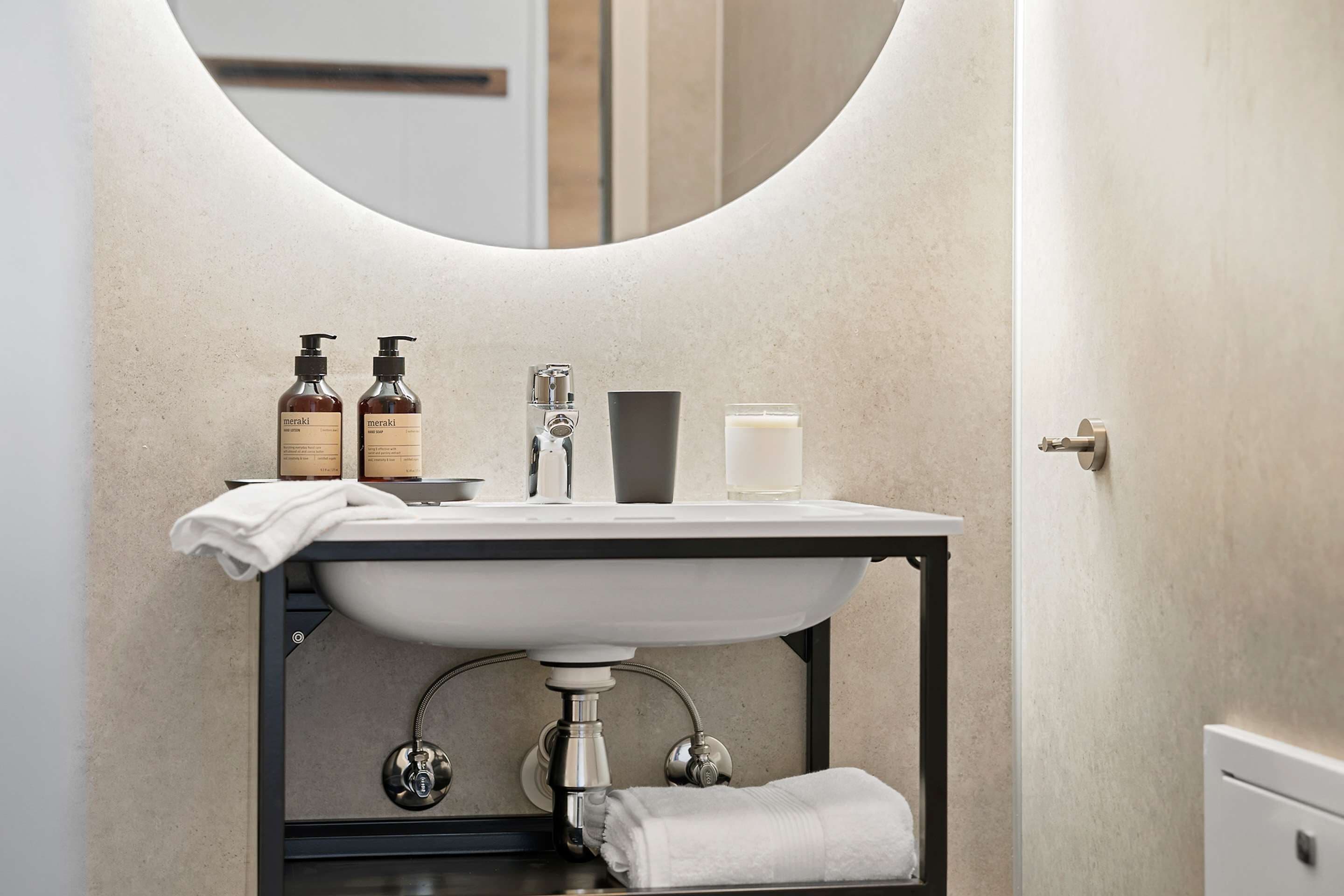 Une salle de bain moderne avec un miroir rond, un lavabo blanc et des articles de toilette.