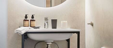 Une salle de bain moderne avec un miroir rond, un lavabo blanc et des articles de toilette.