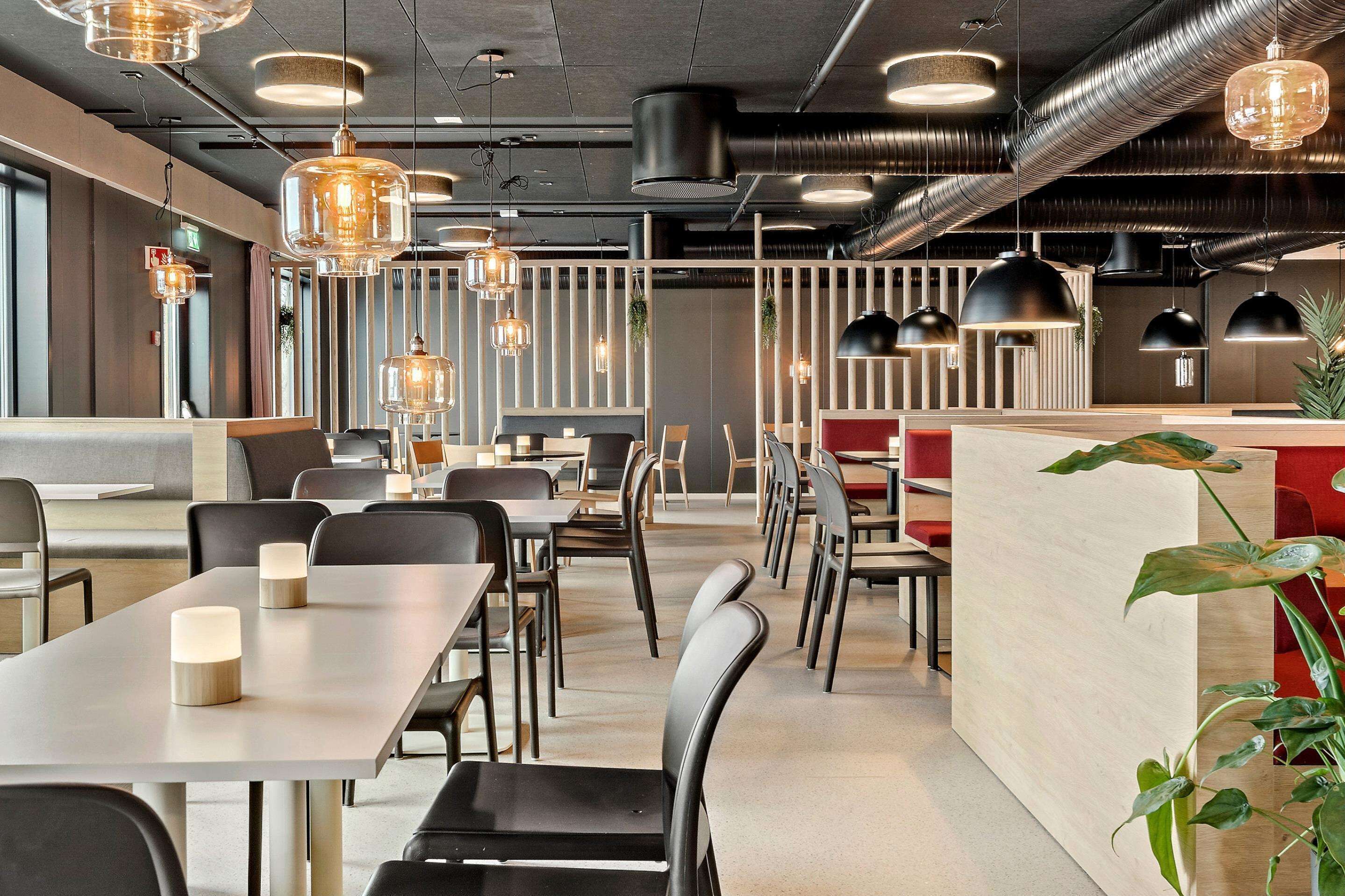 A modern restaurant interior with long tables, black chairs, and pendant lighting.
