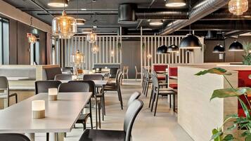 A modern restaurant interior with long tables, black chairs, and pendant lighting.