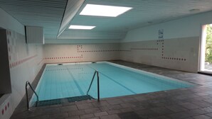 An indoor swimming pool with tiled walls and a tiled floor, a metal pool ladder, and skylights on the ceiling. - Schöne Ferienwohnung App.36 mit Privatstrand (Gambarogno)