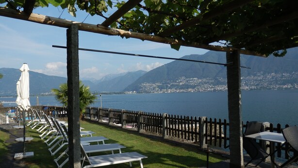 An outdoor seating area with tables and chairs, a pergola, and a view of a lake and mountains. - Schöne Ferienwohnung App.36 mit Privatstrand (Gambarogno)