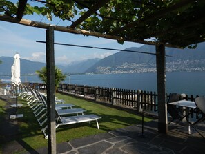 Un espacio al aire libre con mesas y sillas, una pérgola y vistas a un lago y montañas.