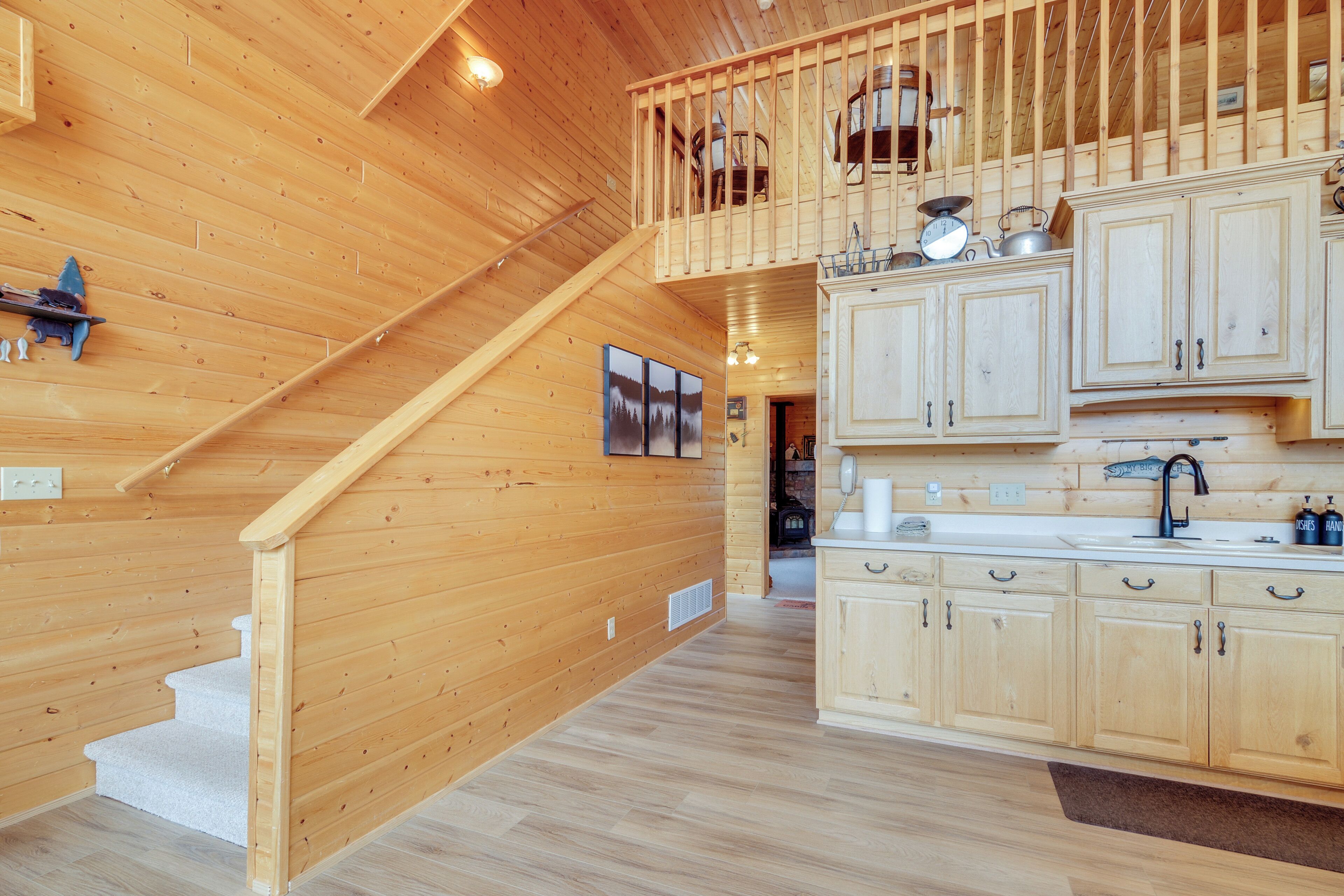 A wooden interior with a kitchen area featuring light-colored cabinets and a staircase leading to an upper level.