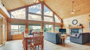 Amplia sala de estar con un techo de madera grande, una chimenea, un televisor y un comedor con una mesa y sillas de madera.