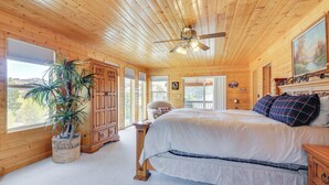 Un dormitorio de cabaña de madera con una cama, un ventilador de techo, un ventanal grande y una planta en maceta.