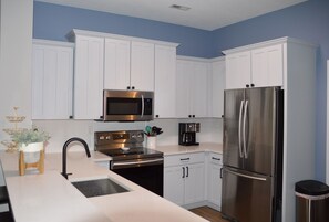 A modern kitchen with white cabinets, stainless steel appliances, and a wooden stool with a plant. - 3 bedroom condo close to Lewes (Lewes)