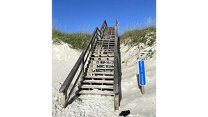 A wooden staircase leading to a beach area with a sign indicating public access.