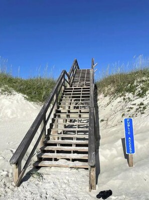 Una escalera de madera que da a una zona de playa, con un cartel que indica acceso público.