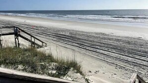 A beach with a wooden staircase leading down to the shore, surrounded by sand and sparse vegetation.
