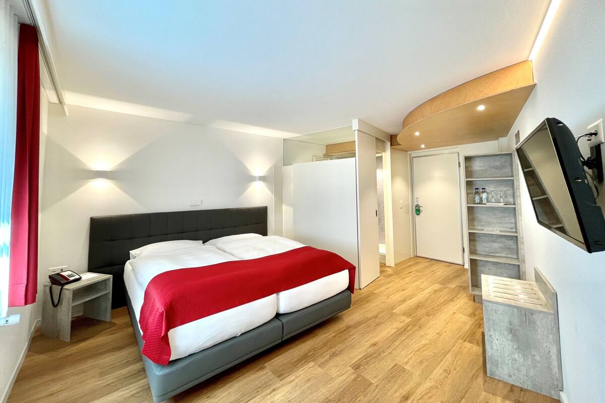 A modern hotel room with a bed, bedside table, and a TV mounted on the wall.