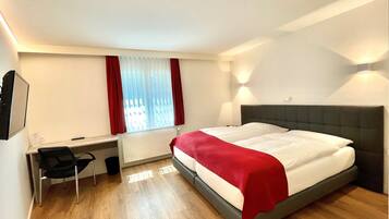 A hotel room with a bed, a desk, a chair, and a window with curtains.