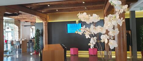 A modern lobby with a wooden ceiling, a digital display, and white orchids.