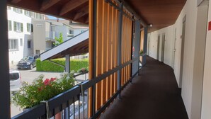Un pasillo con techo de madera, barandilla de metal y vista a coches estacionados y edificios exteriores.