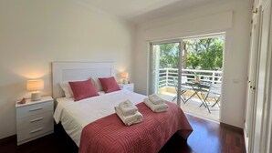 A bedroom with a bed, two bedside lamps, a nightstand, a dresser, and a balcony with a table and chairs. - VILAMOURA CENTRAL 2 WITH POOL  by HOMING (Vilamoura)