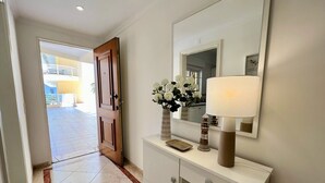 A hallway with a white console table, a mirror, and a door leading to an outdoor area. - VILAMOURA CENTRAL 2 WITH POOL  by HOMING (Vilamoura)