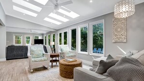 A spacious living room with a ceiling fan, large windows, and a view of the outdoors. - 9 Planters Wood Court at The Sea Pines Resort (Hilton Head Island)