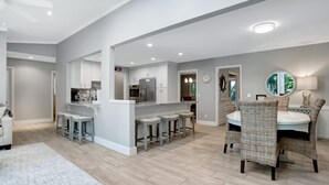 A modern kitchen with a central island, bar stools, and a dining area with wicker chairs. - 9 Planters Wood Court at The Sea Pines Resort (Hilton Head Island)