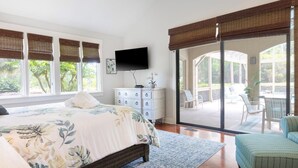 Ein Schlafzimmer mit einem großen Bett, einem Schminktisch, einem Flachbildfernseher und einer Glastür zum Außenbereich.