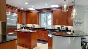 Eine moderne Küche mit Holzschränken, einem Edelstahlkühlschrank und einer großen Kücheninsel mit schwarzer Arbeitsplatte.