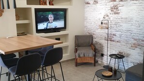 A modern living room with a TV, a wooden dining table, and a brick wall. - Mini Villa (Furiani)