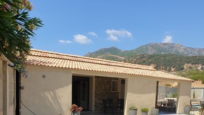 A building with a tiled roof, stone walls, and a patio area with seating and potted plants. - Mini Villa (Furiani)