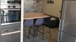 A modern kitchen with a Bosch oven, a Samsung refrigerator, a brick wall, and a wooden dining table with bar stools. - Mini Villa (Furiani)