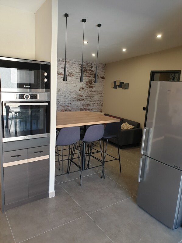 Eine moderne Küche mit Backofen von Bosch, Kühlschrank von Samsung, einer Ziegelwand und einem Holzespeisetisch mit Barhocker.