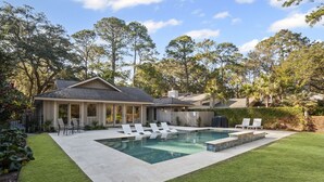Un patio trasero con piscina, sillas de descanso y una casa.