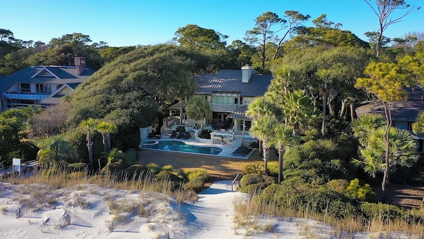 Una grande casa circondata da alberi e da un'area sabbiosa, con una piscina.