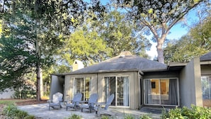 Moderni talo, jossa on katettu terassi, ulkotila istumista varten ja runsaasti vihreää kasvillisuutta.