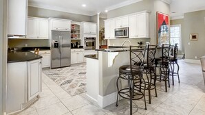Een moderne keuken met witte kasten, roestvrijstalen apparatuur en een centraal eiland met barstoelen.