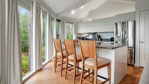 Ett modernt kök med en central köksö, trästolar och stora fönster med gardiner.