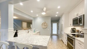 Uma cozinha moderna com armários brancos, uma ilha de mármore e uma ilha central com assentos.