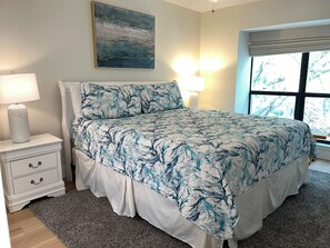 Ein Schlafzimmer mit Bett, Nachttisch, Lampe und Fenster mit Jalousien.