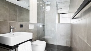 A modern bathroom with a large white bathtub, a glass-enclosed shower, and dark tiled flooring. - Livisit bergpartment 32 - double room 27 sqm - with kitchenette and bathroom (Stuttgart)