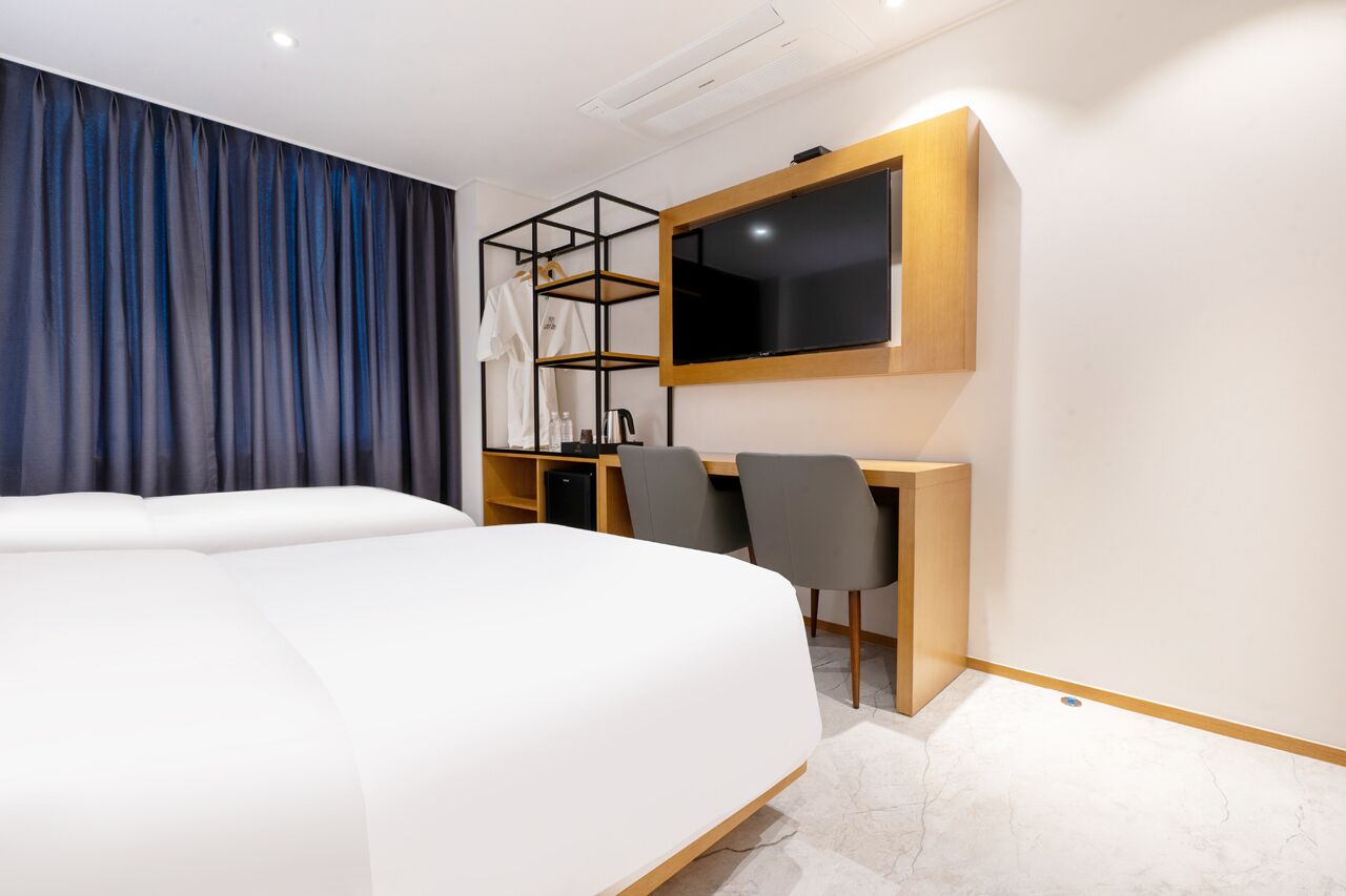 Una habitación de hotel moderna con una cama grande, un escritorio con dos sillas, un televisor y un armario con estantes.