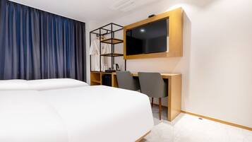 Una habitación de hotel moderna con una cama grande, un escritorio con dos sillas, un televisor y un armario con estantes.