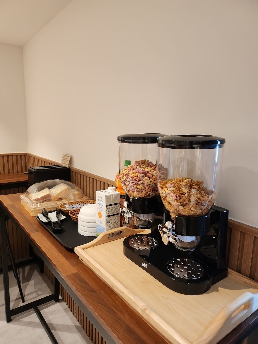 A breakfast bar with two coffee makers, a milk dispenser, and a bread basket.