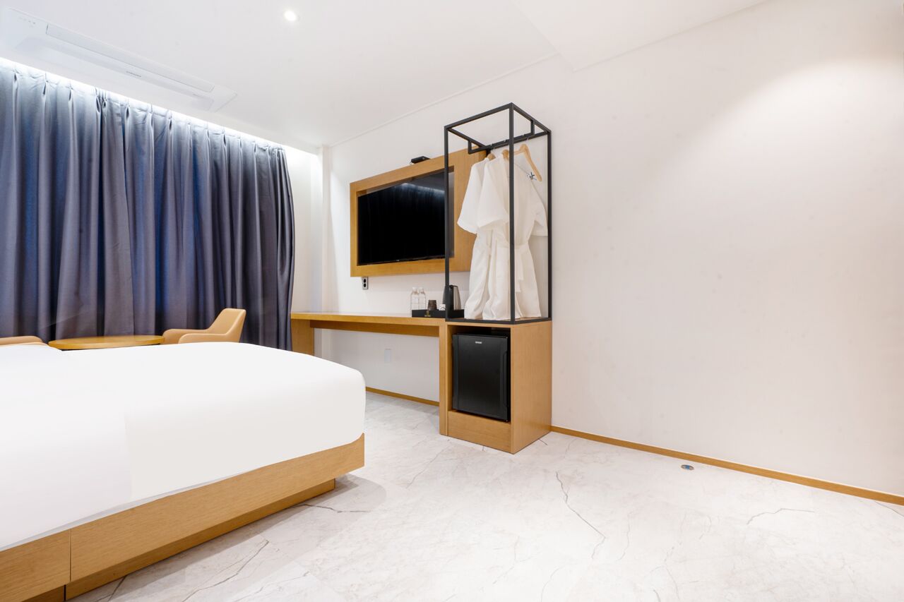 A modern hotel room with a large bed, a desk with a TV, and a robe rack.