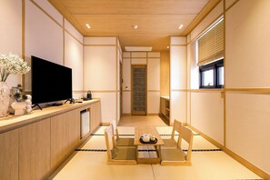 A traditional Japanese-style room with tatami flooring, a television on a wooden console, a sliding door, and a window with blinds. - Daisy Hotel (Yangpyeong)