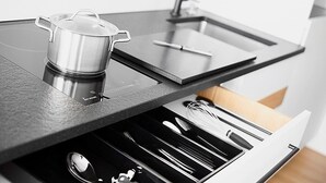 A modern kitchen with a built-in induction cooktop, a stainless steel pot, and a drawer with utensils. - Livisit bergapartment 35 - double room 27 sqm - with south-facing balcony (Stuttgart)