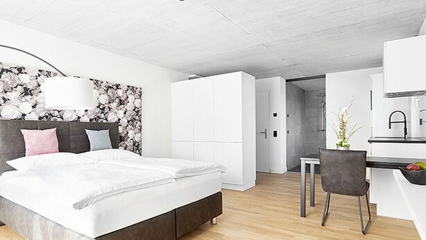 A modern bedroom with a bed, bedside table, and a desk area with a chair. - Livisit bergapartment 35 - double room 27 sqm - with south-facing balcony (Stuttgart)