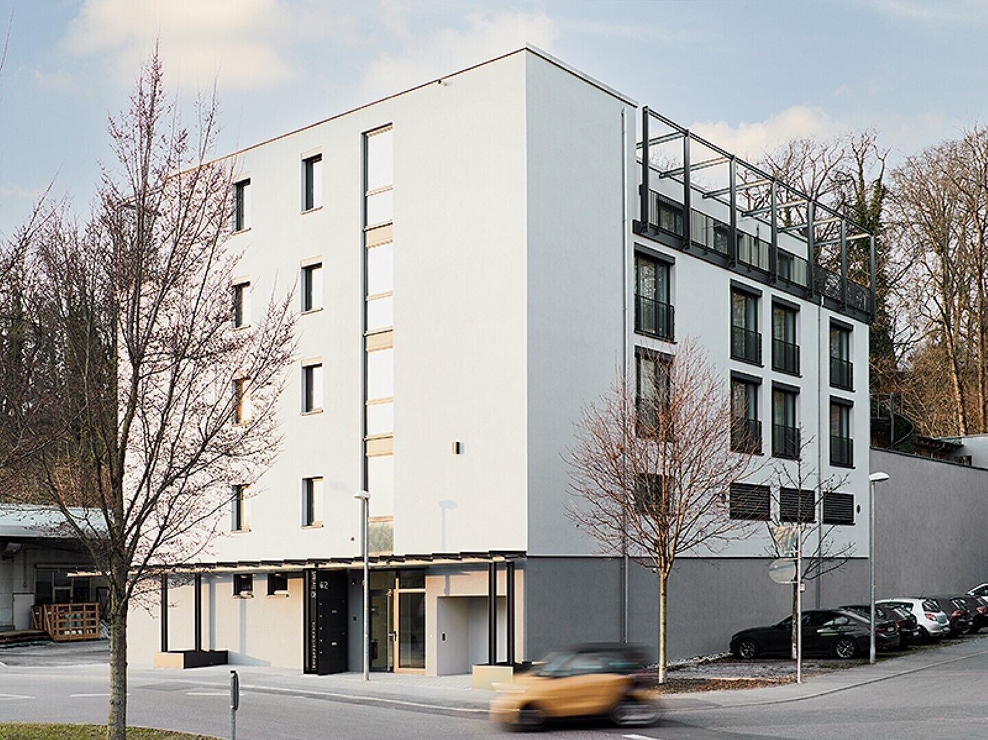 Ein modernes Gebäude mit flacher Fassade, zahlreichen Fenstern und einem Parkplatz mit Autos.