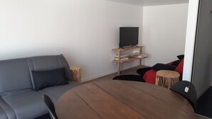 En moderne stue med en grå sofa, et rundt træbord og et fjernsyn på et træskab.