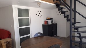 Et spiseområde med et rundt træbord, et sort skab med mikroovn og en trappe med en lampe i hjerteform.