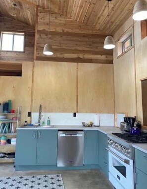 Eine Küche mit Holzbalkendecke, Türkis-Farbenen Schränken, einem Edelstahl-Geschirrspüler, einem Gasherd und Pendelleuchten.