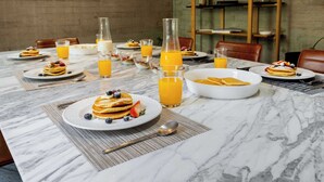 A breakfast setting with plates of pancakes, bowls of cereal, and glasses of orange juice on a marble table.