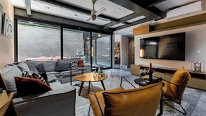 A modern living room with a sofa, armchairs, a coffee table, a flat-screen TV, and a ceiling fan.
